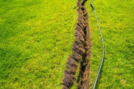 Téléchargez les photos : Auto-installation de l'irrigation avec un arroseur rétractable dans la pelouse finie. Pose de tuyaux d'eau avec pulvérisateurs sous la pelouse pour l'irrigation. - en image libre de droit