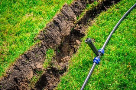 Téléchargez les photos : Auto-installation de l'irrigation avec un arroseur rétractable dans la pelouse finie. Pose de tuyaux d'eau avec pulvérisateurs sous la pelouse pour l'irrigation. - en image libre de droit