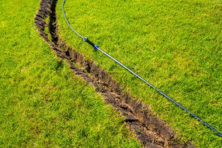 Téléchargez les photos : Un fossé creusé dans la pelouse pour la pose de tuyaux et l'installation d'irrigation. Sol sous pelouse verte et système racinaire - en image libre de droit