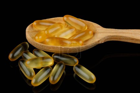 Photo for Omega 3 gelatin capsules in a wooden spoon on a black background - Royalty Free Image