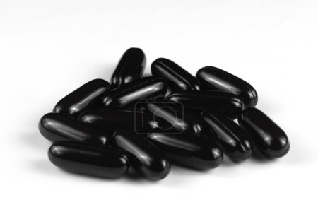 Black gel capsules scattered on a white surface.