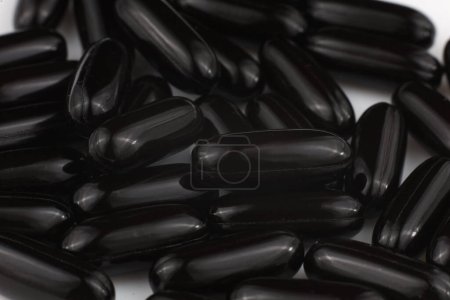 Multiple black gel capsules on a reflective surface.
