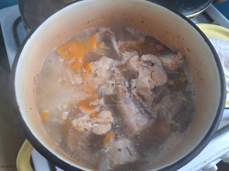 A pot of fish soup boiling with chunks of fish and carrots.