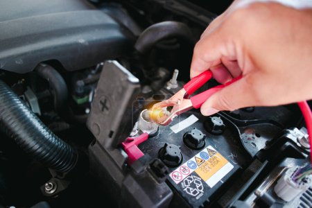 Automechaniker klemmt rote positive Klemmklemme an Autobatterie, Auto-Wartungskonzept