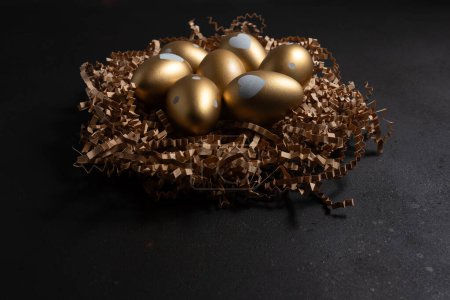 Photo for Golden eggs in paper nest on dark table. - Royalty Free Image