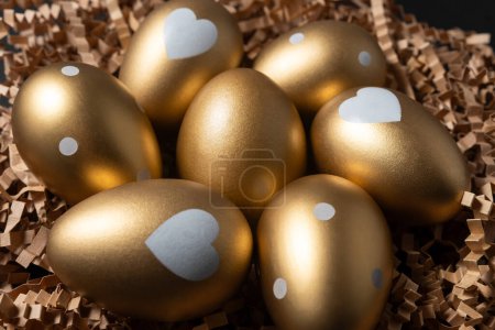 Photo for Close-up view of Golden eggs in paper nest on a dark table. - Royalty Free Image