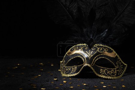 Photo for Carnival gold mask with feathers and confetties on black background. - Royalty Free Image