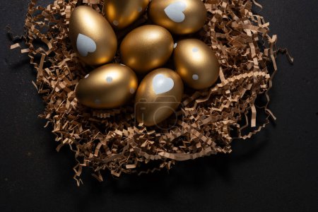 Photo for Gold eggs in paper nest on black background. Top view. - Royalty Free Image