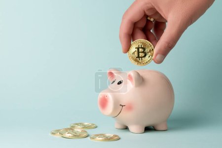 Photo for Minimal investing concept. Hand drops Gold Bitcoin coin into piggy bank on blue background. - Royalty Free Image