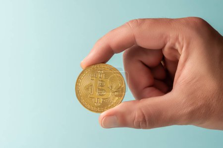Photo for Hand of man holds Bitcoin cryptocurrency gold coin on blue background. Minimal investing concept. - Royalty Free Image