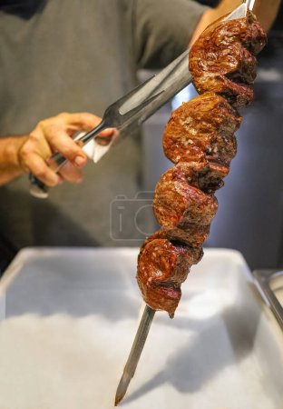 Picanha is a BBQ Steak meat grilled in charcoal. Knife cutting on skewer. Brazilian meat in a Churrascaria restaurant