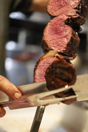 Picanha is a BBQ Steak meat grilled in charcoal. Knife cutting on skewer. Brazilian meat in a Churrascaria restaurant