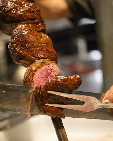 Photo for Picanha is a BBQ Steak meat grilled in charcoal. Knife cutting on skewer. Brazilian meat in a Churrascaria restaurant - Royalty Free Image