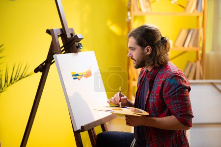 Foto de Un hombre se está enfocando y parece muy feliz mientras pinta algo increíble en un lienzo con muchos colores brillantes. - Imagen libre de derechos