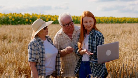 Foto de Family business concept of agriculture old parents farmers and their daughter together analysing the result of harvest from this year using the laptop in the middle of wheat field. Portrait - Imagen libre de derechos