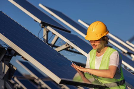 Photo for Smiling happy lady at photovoltaic solar farm she carefully check the cleanliness of the photovoltaic solar panels she wearing safety equipment. - Royalty Free Image
