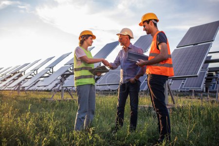 Photo for Ecological innovation and green energy concept at photovoltaic solar farm the ecological engineer old man and two his assistant discussing about the solar panels using the digital tablet. Portrait - Royalty Free Image