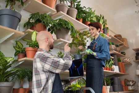 Photo for In front of the camera shop assistant man together with the florist woman working together they checking the inventory from the shop using the laptop and discussing at the same time. Portrait - Royalty Free Image