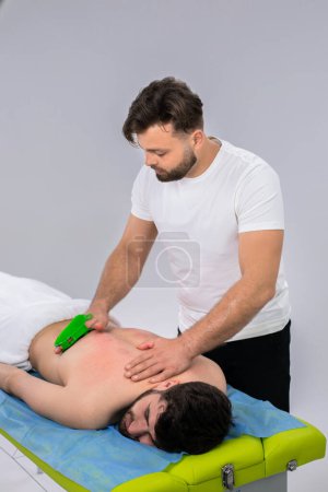 Téléchargez les photos : Professional therapist at medical clinic doing back massage for muscles with a special accessories while client man are laying down on the massage table. Portrait - en image libre de droit
