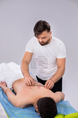 Téléchargez les photos : Thérapeute professionnel à la clinique médicale faisant massage du dos pour son client il en utilisant des accessoires spéciaux pour cela. - en image libre de droit