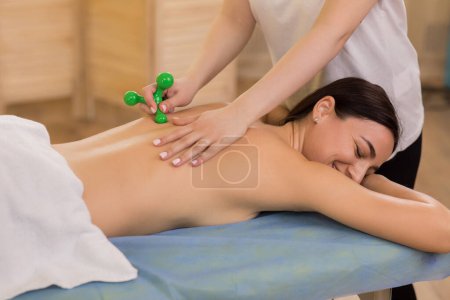 Téléchargez les photos : Salle de massage professionnelle la thérapeute femme utilisant des accessoires de massage spéciaux pour un client heureux revitalisant massage du dos allongé sur la table de massage. - en image libre de droit