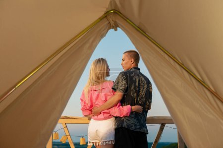 Téléchargez les photos : Très beau couple sont embrasser à l'extérieur d'une tente et admirer eachother et converser comme ils regardent à l'extérieur du paysage étonnant de la nature qui a des montagnes et des forêts. Portrait - en image libre de droit