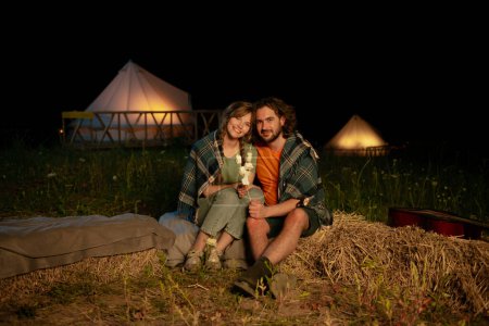 Téléchargez les photos : Portrait de jeune couple assis près du feu de camp sur la plage la nuit d'automne. - en image libre de droit