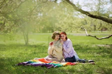 Foto de Bonita dos lesbianas tienen un picnic en el parque acostado en la manta y discutir la celebración de la bandera lgbt en la parte posterior. - Imagen libre de derechos