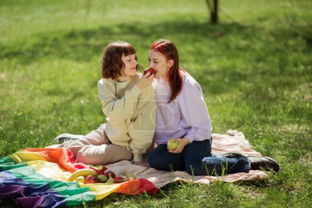 Téléchargez les photos : Belle deux lesbiennes dans le parc ont un pique-nique ils mangent ensemble une pomme et profiter du soleil ensemble. - en image libre de droit