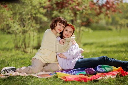 Foto de En un día soleado pareja lesbiana muy carismático acostado en la hierba y mirando por encima del concepto de tableta digital de estilo de vida lgbt. - Imagen libre de derechos