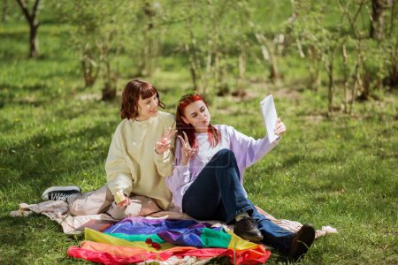 Photo for Good looking two ladies lesbian in the park laying down on the blanket and take some pictures for memories using the digital tablet they are smiling and feeling so happy kissing each other. Lgbt - Royalty Free Image