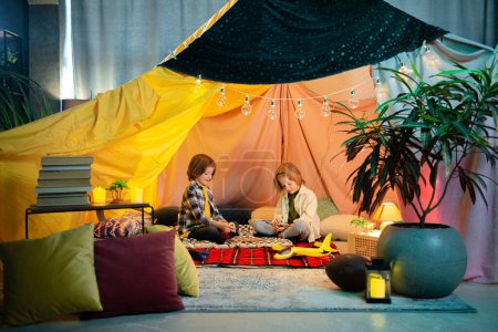 Photo for Two boys are laughing and playing together inside a big comfy tent, they re having a lot of fun. - Royalty Free Image