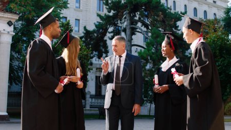 Photo for Happy college professor congratulated his students on their graduation day in the college garden all together are excited holding their diplomas. - Royalty Free Image