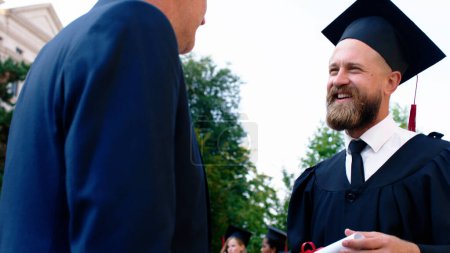 Photo for Emotional day for father and son on the graduation they posing together in front of the camera while holding diploma. - Royalty Free Image