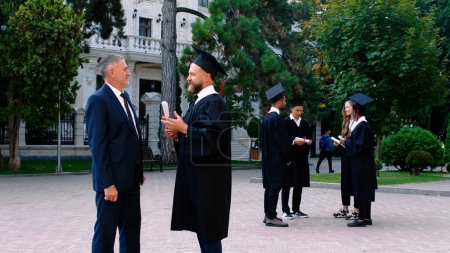 Photo for Closeup to the camera charismatic graduate man have a conversation with his dad very excited and happy on his graduation day. - Royalty Free Image
