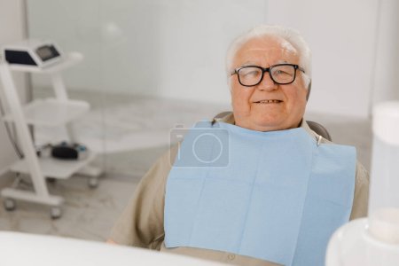 Téléchargez les photos : Concept de soins de santé chez le dentiste le vieil homme patient posant devant la caméra avec un grand sourire assis sur la chaise du dentiste. - en image libre de droit