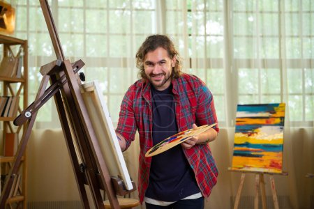 Téléchargez les photos : Un peintre très heureux regarde sa toile qu'il vient de peindre et ajoute quelques touches de finition il est très heureux avec son travail. - en image libre de droit