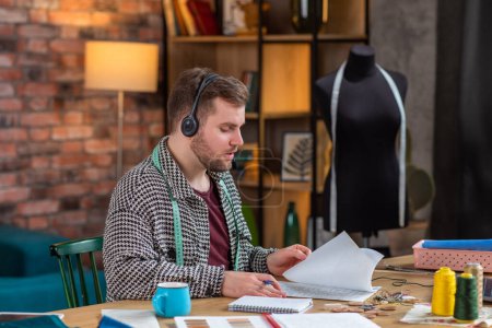Photo for In front of the camera at tailoring atelier good looking man tailor speaks using the headphones with some customer he take the online order. - Royalty Free Image