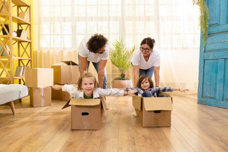 Photo for In front of the camera after young family moving to new home they take their kids and put them on the boxes and start to doing a ride through the living room. Family - Royalty Free Image