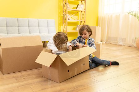 Photo for Portrait of two boys playing in cardboard boxes while family moving to new house, copy space. Family - Royalty Free Image