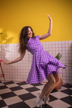 Foto de Feliz y emocionada jovencita bailando en la cocina delante de la cámara saltando y partiendo las piernas al final y sonriendo a lo grande. - Imagen libre de derechos