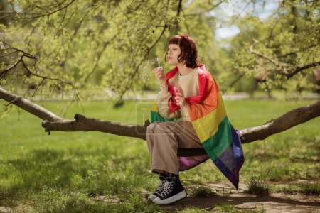 Photo for At nature lady take a sit on a tree she makes some soap bubbles and feeling so happy she holding the lgbt flag on the back. lgbt - Royalty Free Image