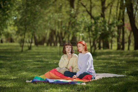 Photo for Perfect sunny day in the middle of nature lesbian couple posing in front of the camera while holding the lgbt flag they are so cute together. Lgbt - Royalty Free Image