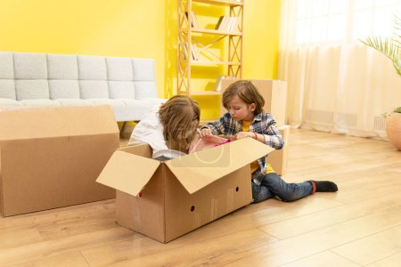 Photo for Happy little kids children enjoying moving day, playing in new home together, preschool boy and 8s girl having fun with cardboard boxes, express delivery, relocation and renovation concept. Family - Royalty Free Image