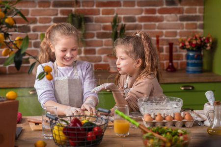 Foto de Amazing and happy two sisters cute girls have fun time at the kitchen island together preparing the dough to cook a delicious dessert. - Imagen libre de derechos