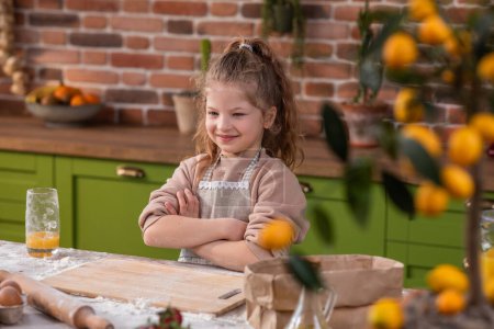 Photo for Posing in front of the camera good looking little girl crossing hands and looking straight have a pretty smile at the kitchen island. - Royalty Free Image