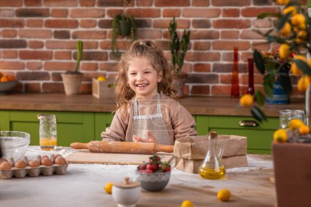 Photo for Rustic kitchen island pretty and smiling large very excited little girl dancing while preparing some dessert at the kitchen island at home. - Royalty Free Image