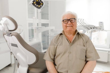 Téléchargez les photos : Un vieil homme séduisant, patient, est venu faire un examen dentaire à la clinique dentaire où il posait devant le gros plan de la caméra en attendant le dentiste. Dentiste - en image libre de droit