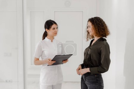 Téléchargez les photos : Superbe de voir deux assistantes médicales se promener dans la clinique médicale et discuter de quelque chose qu'elles regardent sur une carte et analysent quelque chose devant la caméra. Hôpital - en image libre de droit