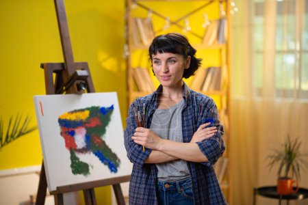Foto de Una foto baja de una artista de pelo corto pintando algo muy chic y moderno con su pincel sobre un lienzo frente a ella. - Imagen libre de derechos